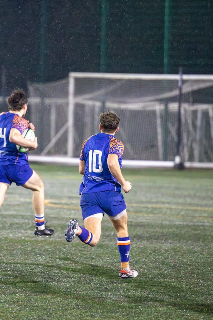 Rugby players in action during a match on a rainy field in England.